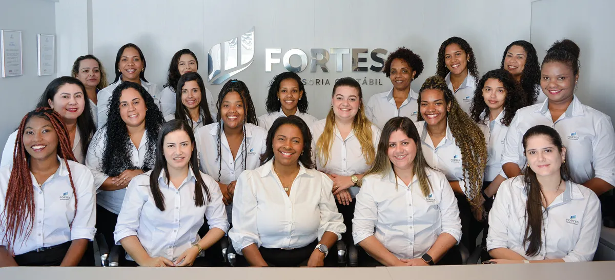 Equipe da Fortes Assessoria Contábil reunida no escritório, diante do logotipo da empresa